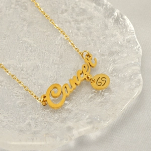 Golden stainless steel Cancer zodiac necklace with letter pendant on glass tray
