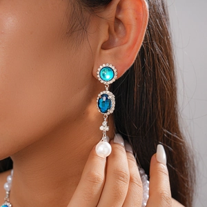 Close-up of elegant long drop earrings featuring blue gems, rhinestones, and white pearls