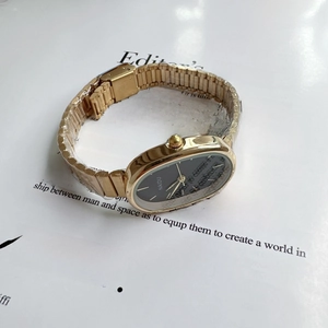 Detail of small oval black dial watch with gold metal strap on editorial magazine