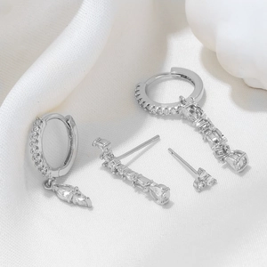Detailed view of silver hoop earrings and zircon studs on white silk fabric