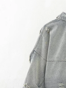 Detail of distressed grey denim jacket showing ripped shoulders and frayed edge textures