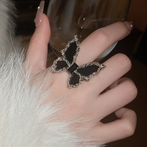 Detail of silver butterfly ring with black wings inlay worn by a model in a cozy setting