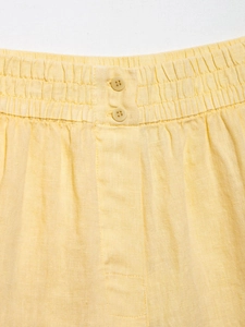 Detail of yellow linen shorts featuring a double-button waist and elastic waistband design