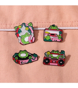 Detail of four green frog enamel pins with pink music theme on denim background