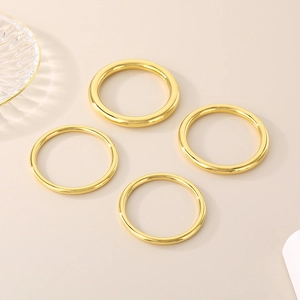 Detailed view of four polished gold hollow tube bangles made of stainless steel