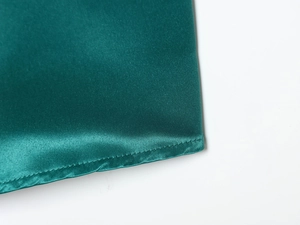 Dettaglio dell'orlo del vestito in raso verde smeraldo con cuciture fini e trama di seta