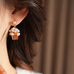 Macro shot of quirky popcorn bucket earrings with pearls and gold accents worn by a model