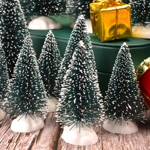 Miniature green Christmas pine trees with snow effect on wooden table with gift boxes