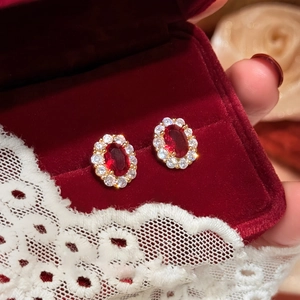 Close-up of vintage oval red gemstone earrings with white zircon halo in a velvet box