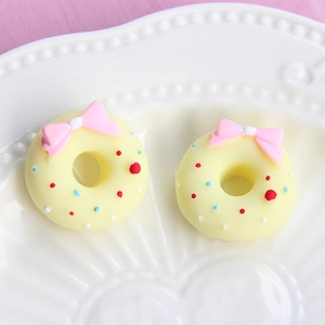 Macro shot of two resin donut charms with pink bows and colorful sprinkles on a tray