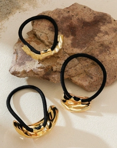 Close-up of three gold irregular wave metal charms on black elastic hair ties on stone