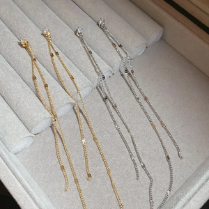 Detailed close-up of gold and silver tassel chain earrings with cubic zirconia in a gray box