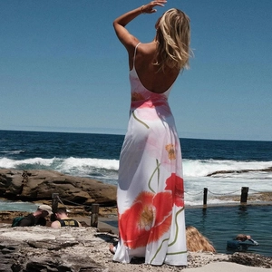 Detail showing backless white long dress with red floral print against seaside backdrop