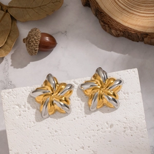 Gros plan de boucles d'oreilles étoiles bicolores or et argent sur fond de pierre blanche