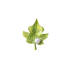 Detail of green leaf brooch with enamel texture and central pearl on white background