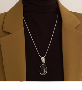 Detail of French vintage resin oval pendant on silver snake chain over a sweater