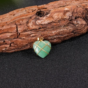 Vista macro di ciondolo a cuore in avventurina verde avvolto in filo d'oro su legno naturale