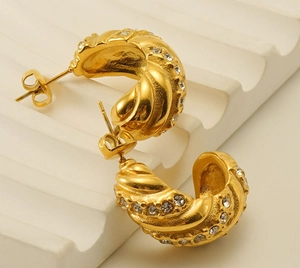 Vue détaillée de boucles d'oreilles torsadées dorées en C avec sertissage de zircons