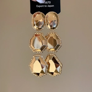Gros plan détaillé de boucles d'oreilles géométriques dorées à trois couches de métal poli