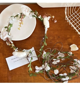 Close-up of white fabric flowers and green leaves on a woven vine headband accessory