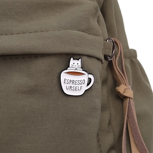 Detail of Espresso Urself cat in coffee cup enamel pin on an olive canvas backpack
