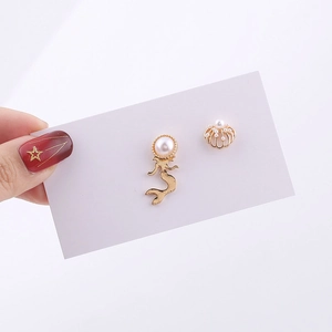 Detail view of gold mermaid and shell stud earrings with white pearl accents