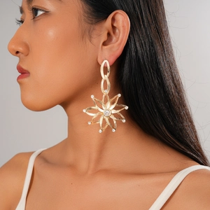 Detailed close-up of a large gold hollow flower earring with crystals on a female model