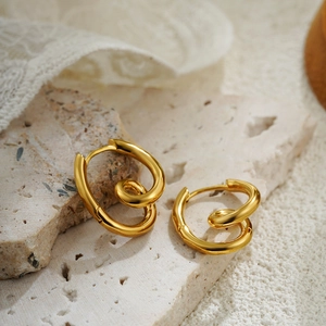 Detail view of 18K gold spiral hoop earrings on a textured stone base with lace decor