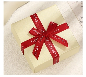 Close-up of a pale yellow jewelry gift box with a red ribbon and white Crystal text
