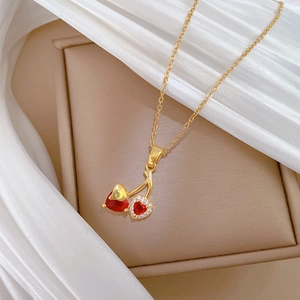 Detailed close-up of a gold cherry pendant necklace with red heart crystals on white silk