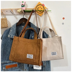 Detailed view of brown and beige corduroy tote bags with front pockets hanging on wood hook