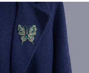 Vue détaillée d'une broche papillon en strass verts fixée sur le revers d'un manteau en laine