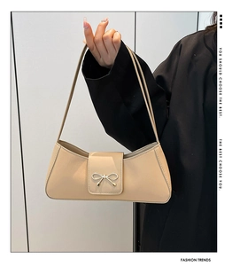 Detailed close-up of beige leather shoulder bag with golden bow hardware on black blazer