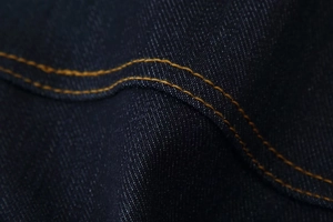 Gros plan détaillé du tissu denim bleu foncé avec des surpiqûres orange classiques