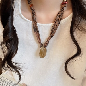 Detail of fabric paisley necklace with large amber resin teardrop pendant on white clothing