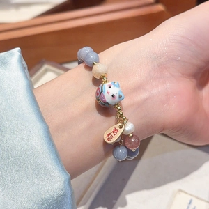 Dettaglio macro del ciondolo Maneki Neko e targhetta 'Fu' su bracciale perle