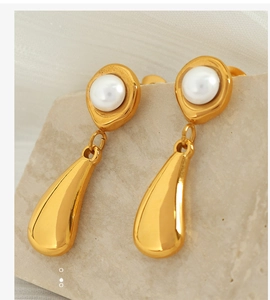 Macro shot of gold teardrop earrings with white pearls on a light stone background