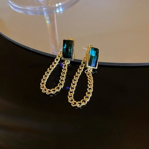Détail de boucles d'oreilles pendantes en pierre émeraude avec chaînes dorées sur miroir noir