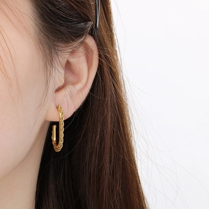 Close-up of gold U-shaped twist hoop earrings with textured rope design on a model