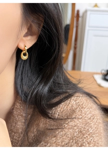 Goldene strukturierte ovale Creolen an einem Model mit braunem Pullover