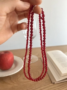 Close-up of red agate beaded necklace with silver clasp held over a wooden table