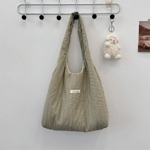 Close-up of olive green pleated tote bag with a white plush lamb keychain on a metal hanger