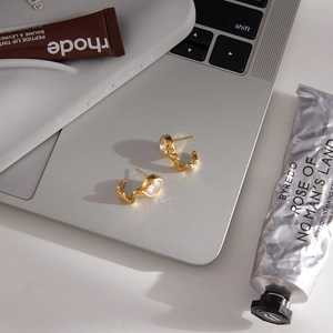 Elegant gold wave stud earrings with round zircon stones on a sleek silver laptop surface