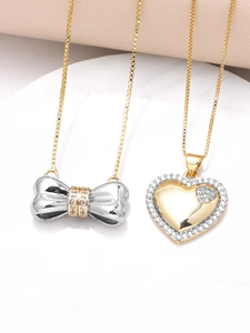 Macro shot of gold heart and bow pendants with sparkling zircons on marble surface
