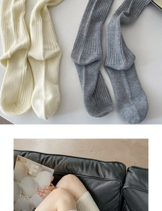 Close-up of thick knitted knee-high socks in cream and grey colors with ribbed texture