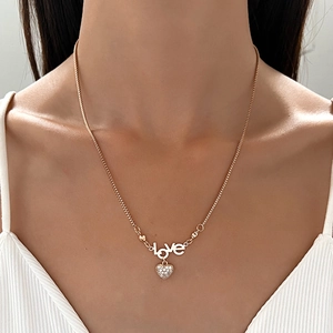 Golden necklace with LOVE lettering and a sparkling heart pendant worn by a model