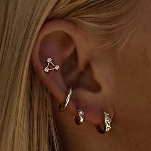 Gold sunburst star hoop earrings and studs set with crystals on a model's ear