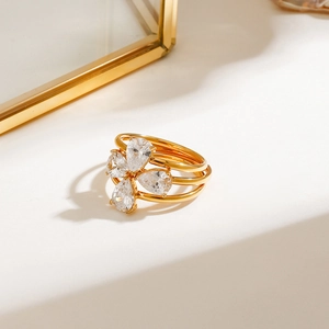 Macro detail of a triple-layered gold band ring with floral zircon stones on white surface