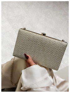 Detail of a golden chevron acrylic clutch bag with a sleek metallic chain strap