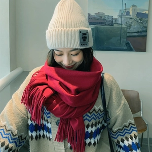 Close-up of red fringed wool scarf paired with a beige knit beanie for winter styling